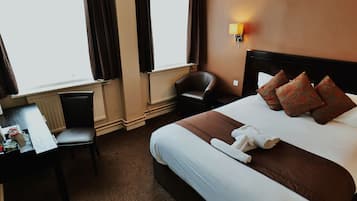 Ein Hotelzimmer mit Bett, Schreibtisch, Stuhl und einem fensterbepflanzten Fenster.