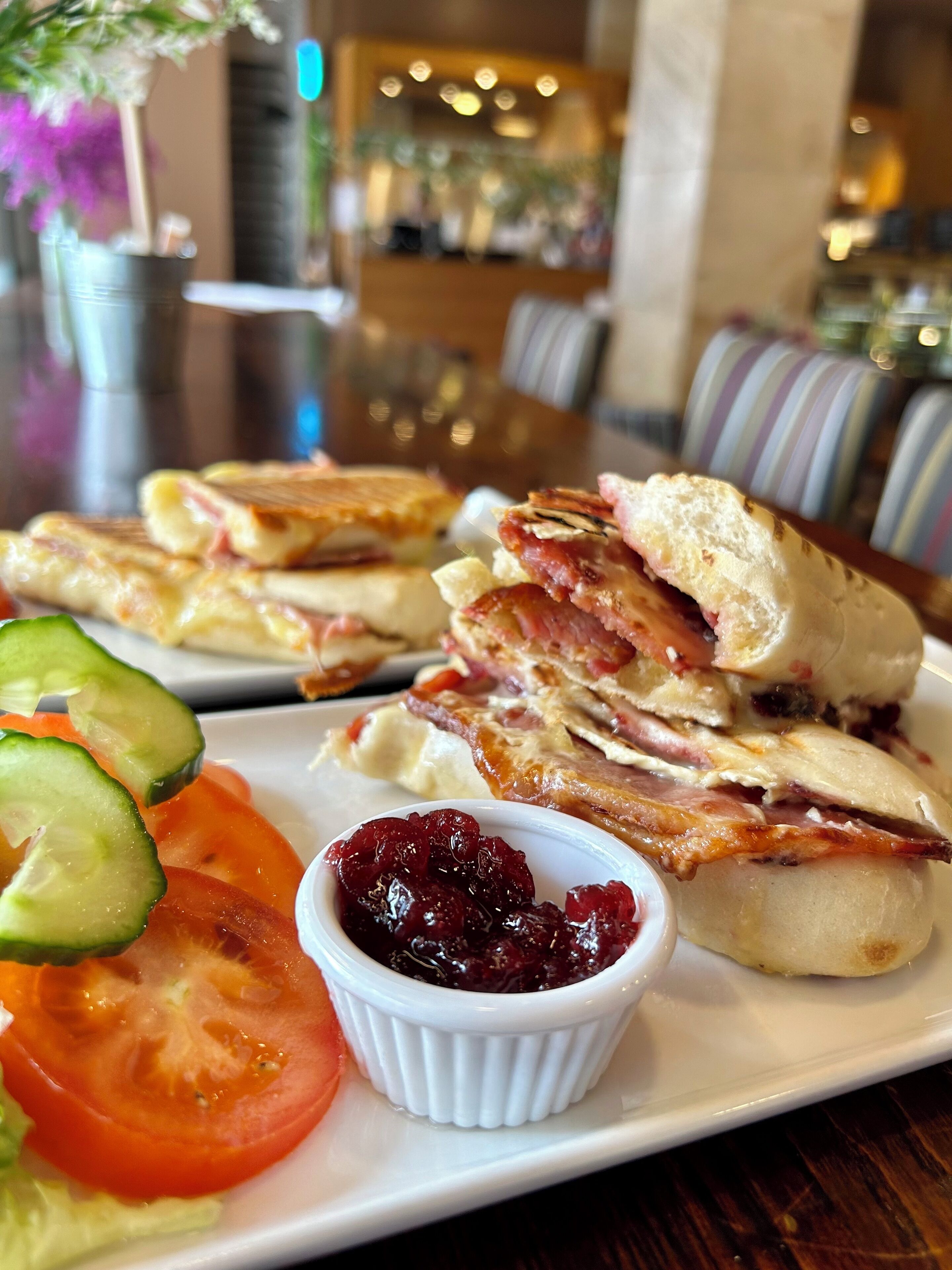 A plate with sandwiches, cucumber slices, tomato slices, and a small bowl of cranberry sauce.