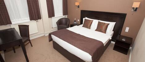 A hotel room with a large bed, two bedside tables, a chair, and a desk.