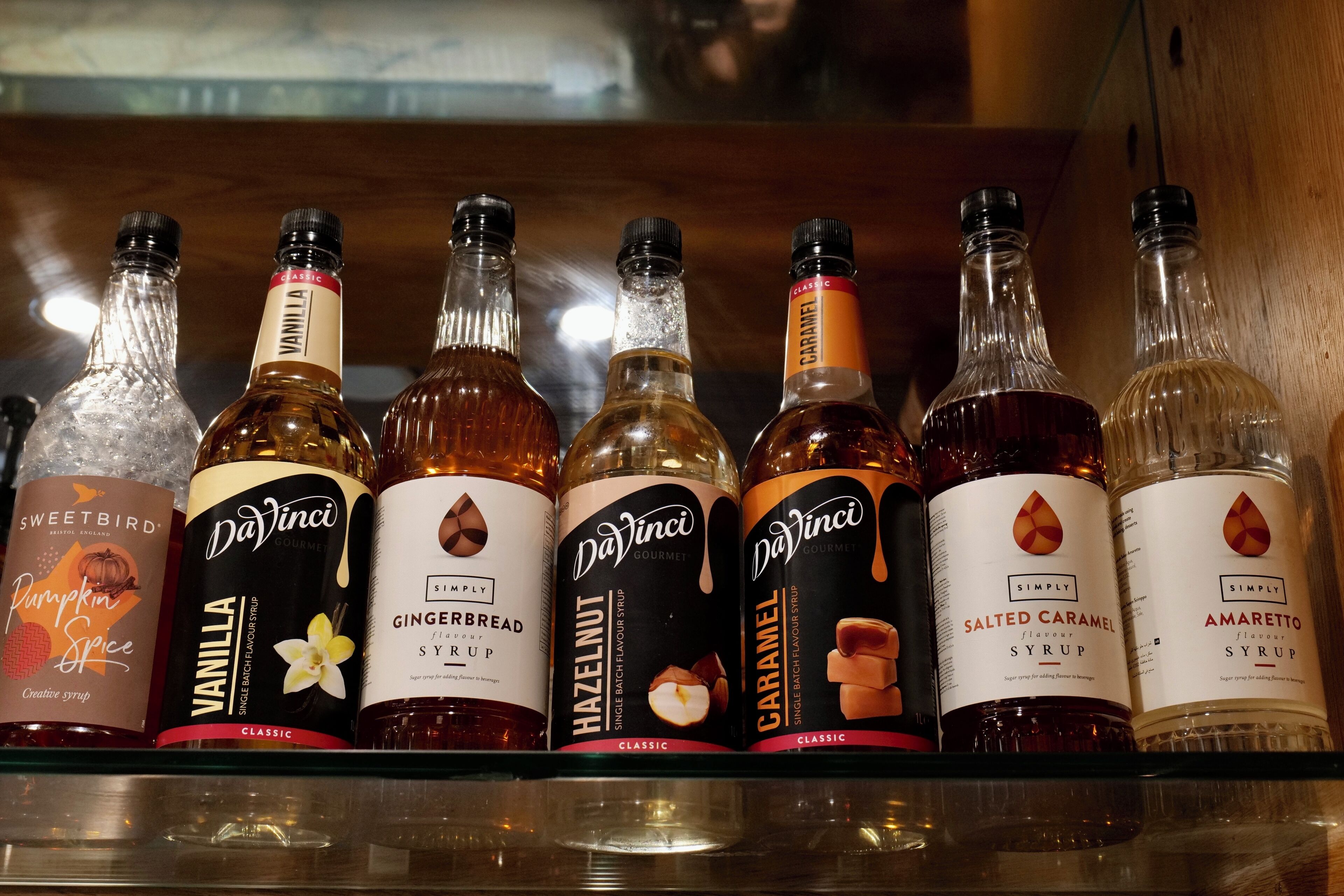 Una estantería con varias botellas de sirope, incluyendo los sabores vainilla, jengibre, avellana, caramelo, caramelo con sal y amaretto.