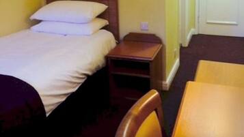 A single bed with white bedding, a wooden nightstand, and a wooden chair in a room with yellow walls.