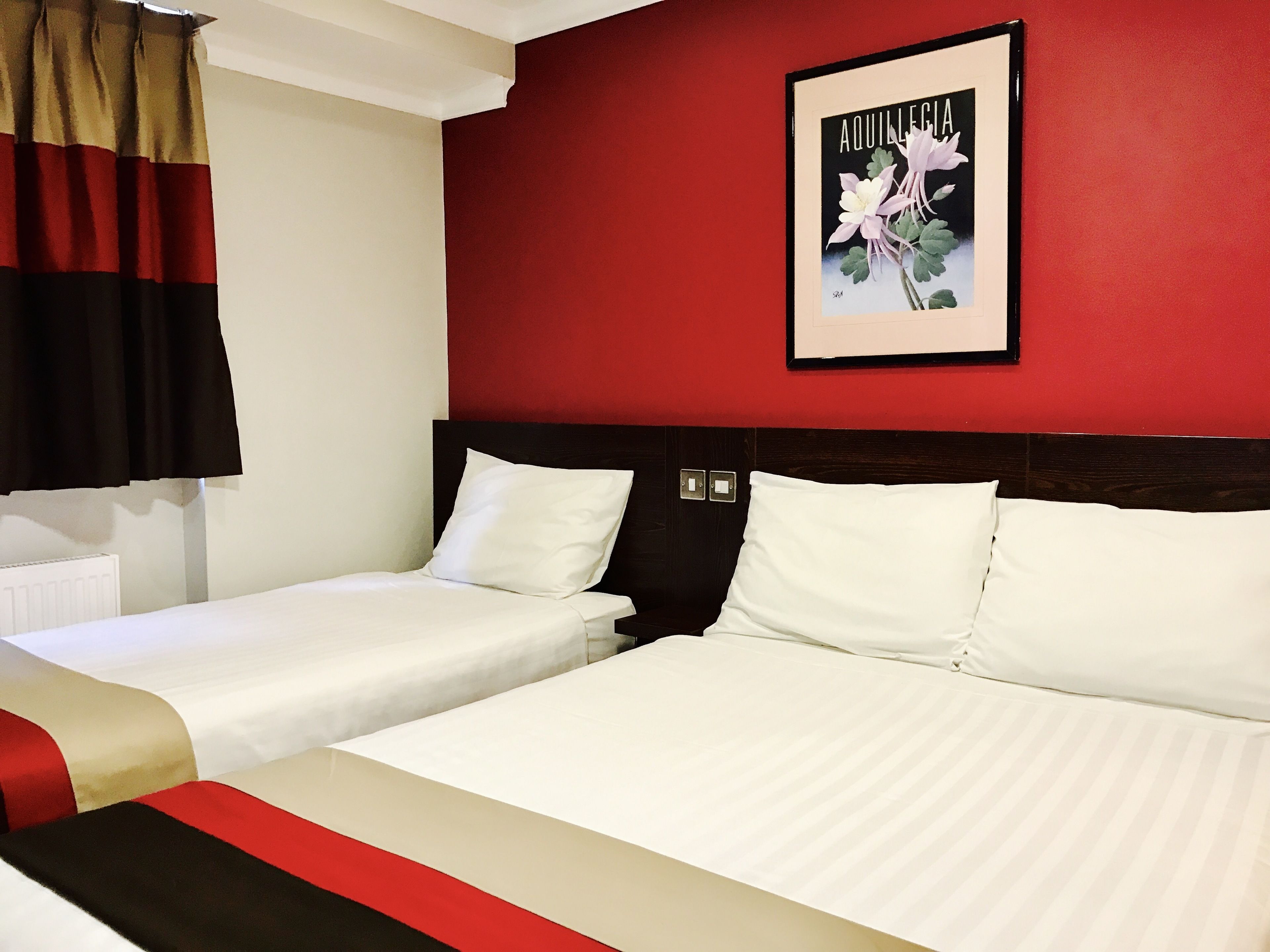 Habitación de hotel con dos camas, una pared de acento roja e impresión botánica enmarco.