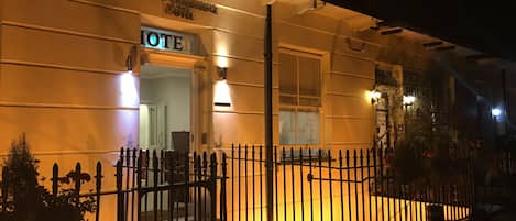 El exterior del Hotel Royal Cambridge de noche, con una entrada bien iluminada, una cerca de metal y un cartel.