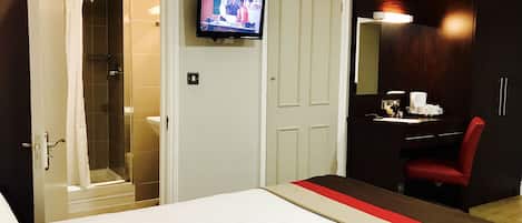 A hotel room with a bed, a television mounted on the wall, a desk with a chair, and a shower area.