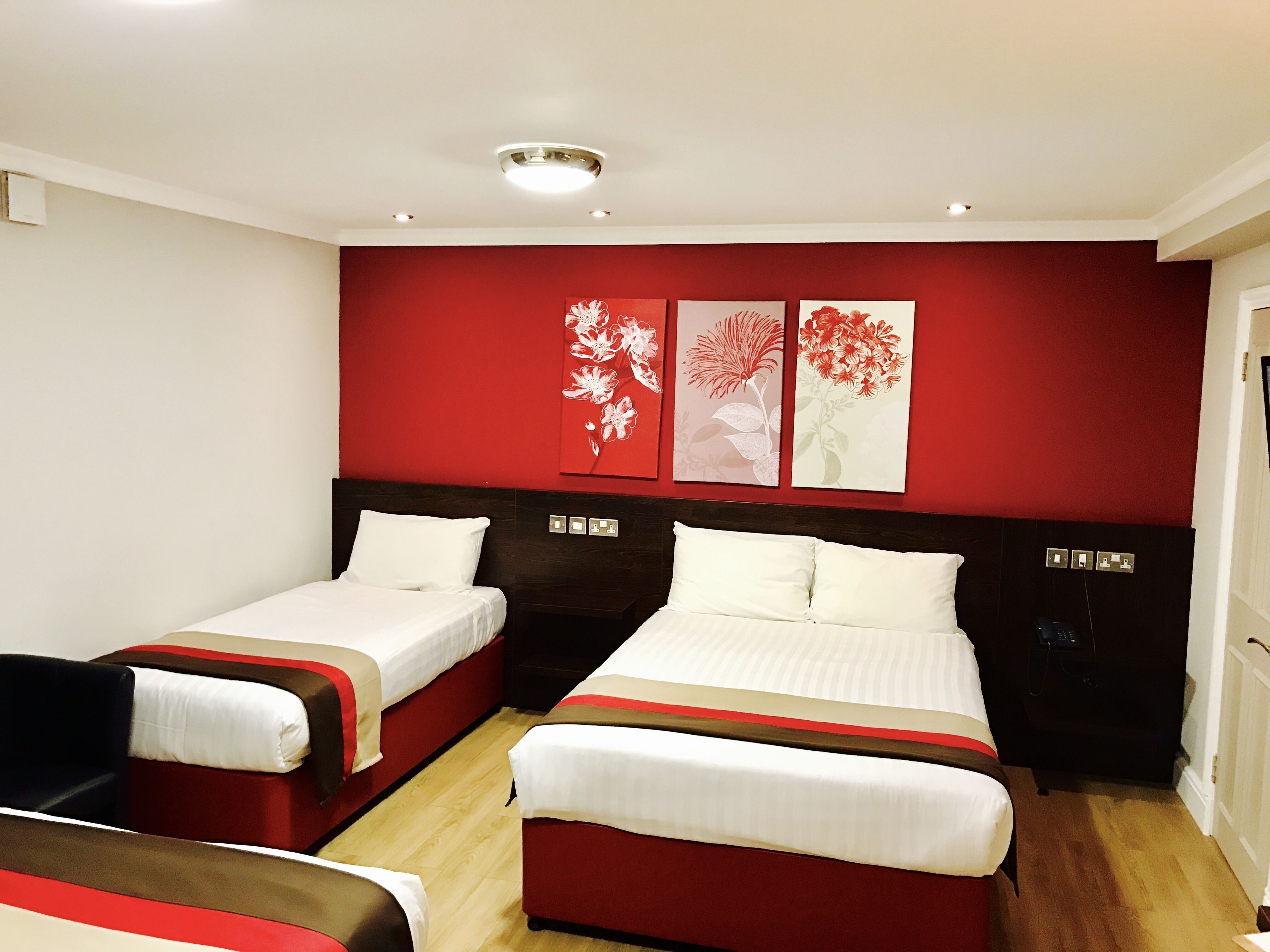 A hotel room with two beds, a red accent wall, and a ceiling light.