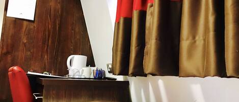 A hotel room with a bed, a desk with a coffee cup, a remote control, and a red chair.