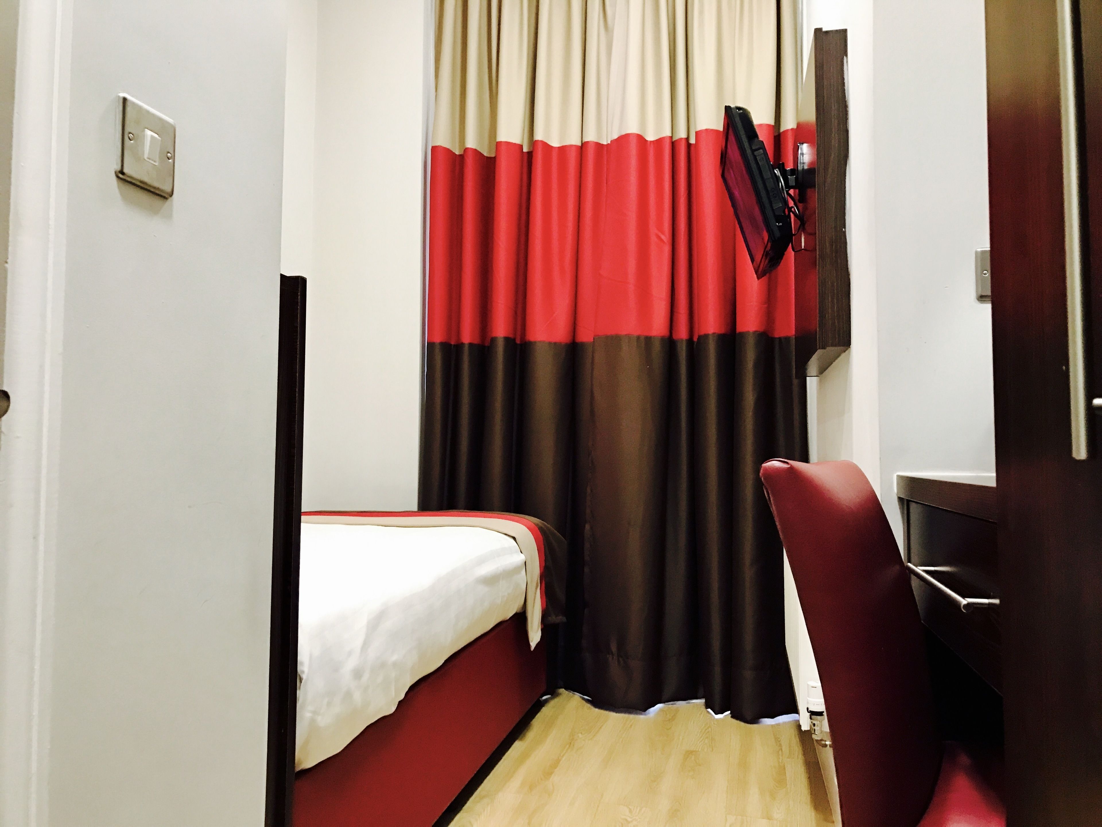 Een kleine, compacte hotelkamer met een enkel bed, een bureau en een stoel.