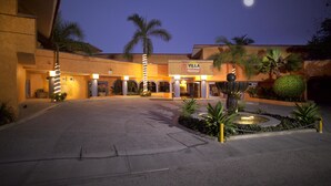 Fachada de hotel bien iluminada, con palmeras y una fuente.