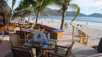 Un restaurante frente a la playa con terraza, palmeras y vistas al mar.