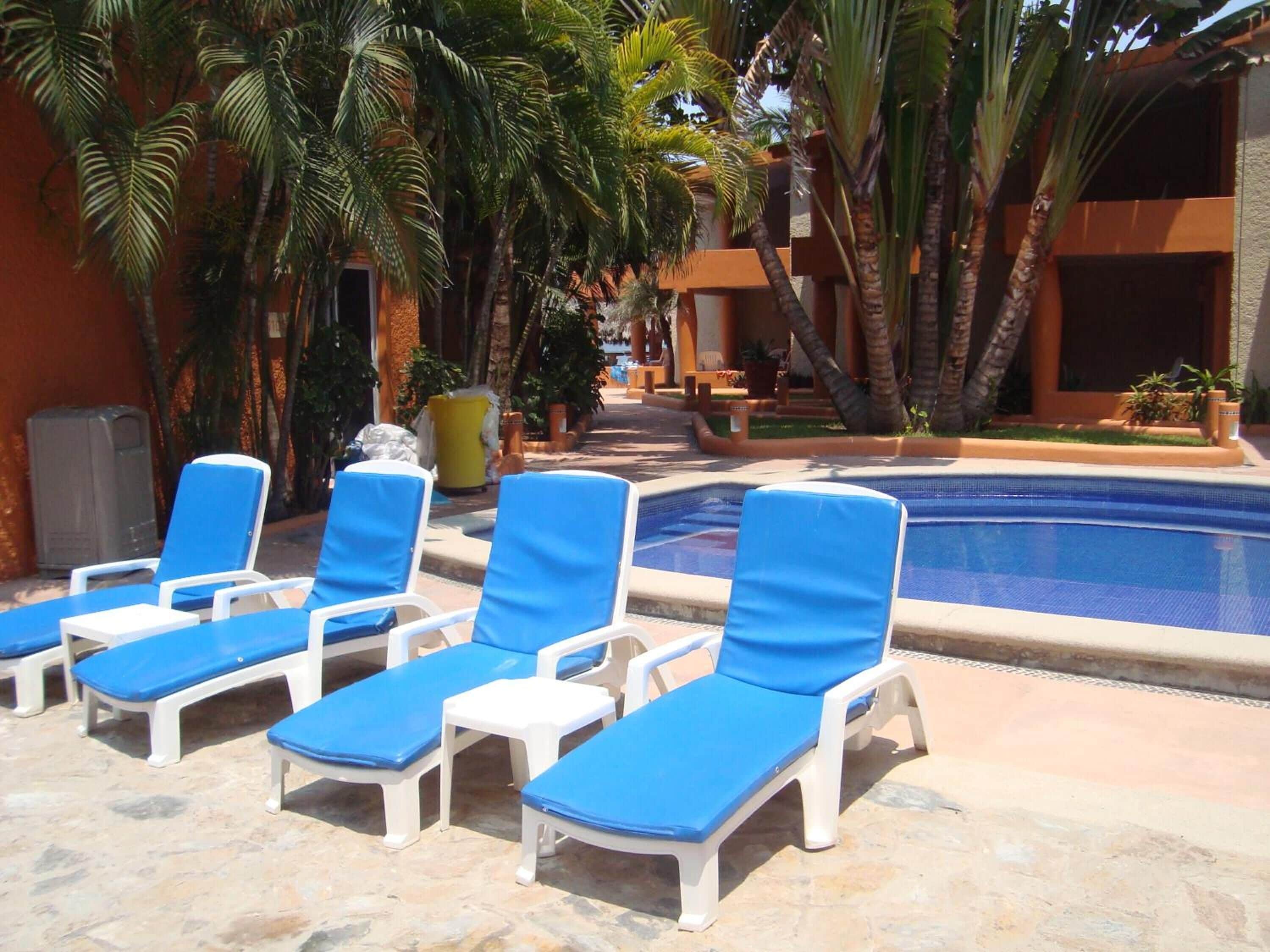 Uma área à beira da piscina com espreguiçadeiras e palmeiras.