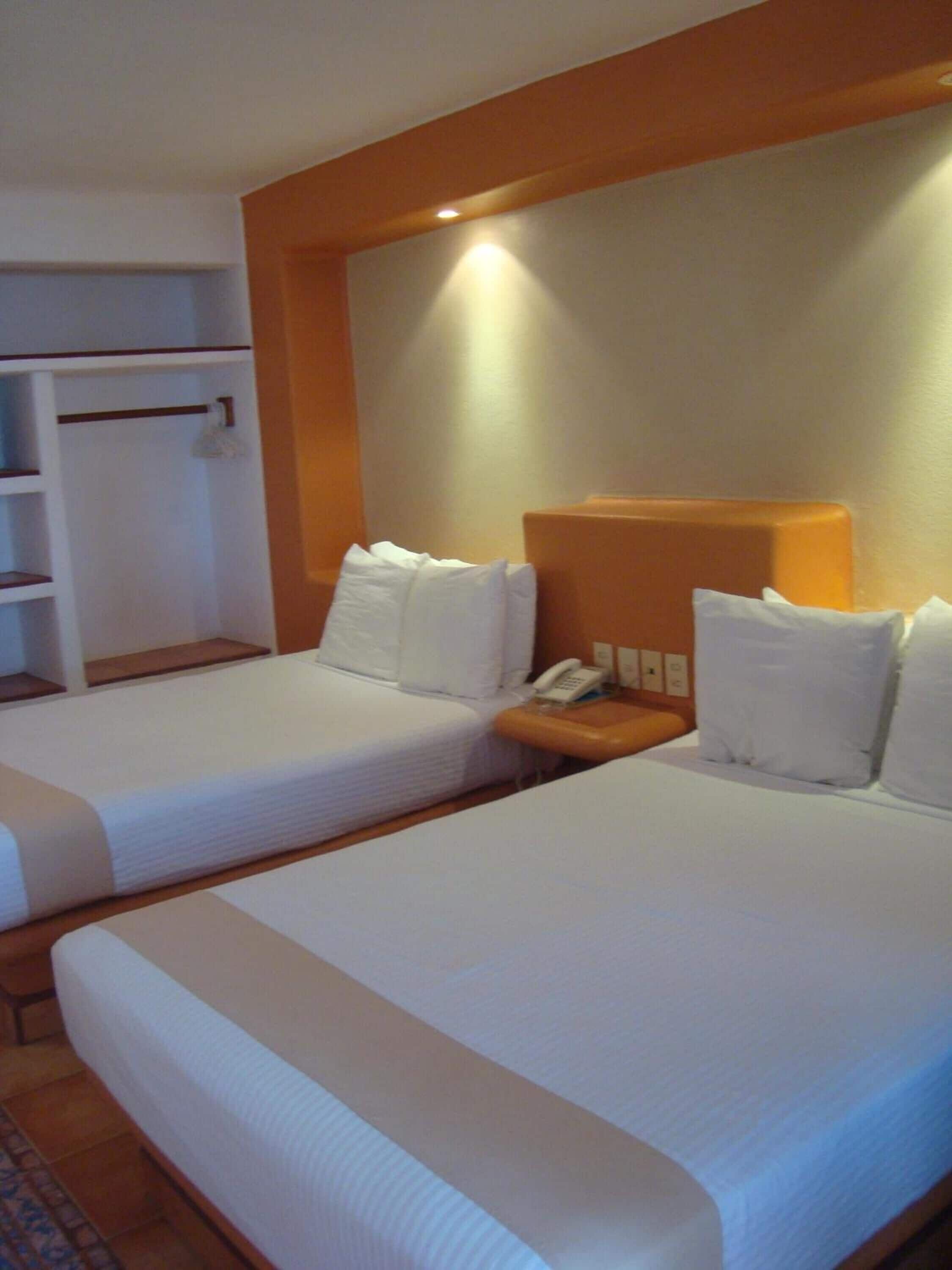 Une chambre d’hôtel avec deux lits, une table de chevet avec un téléphone et une armoire avec une tringle pour suspendre les vêtements.