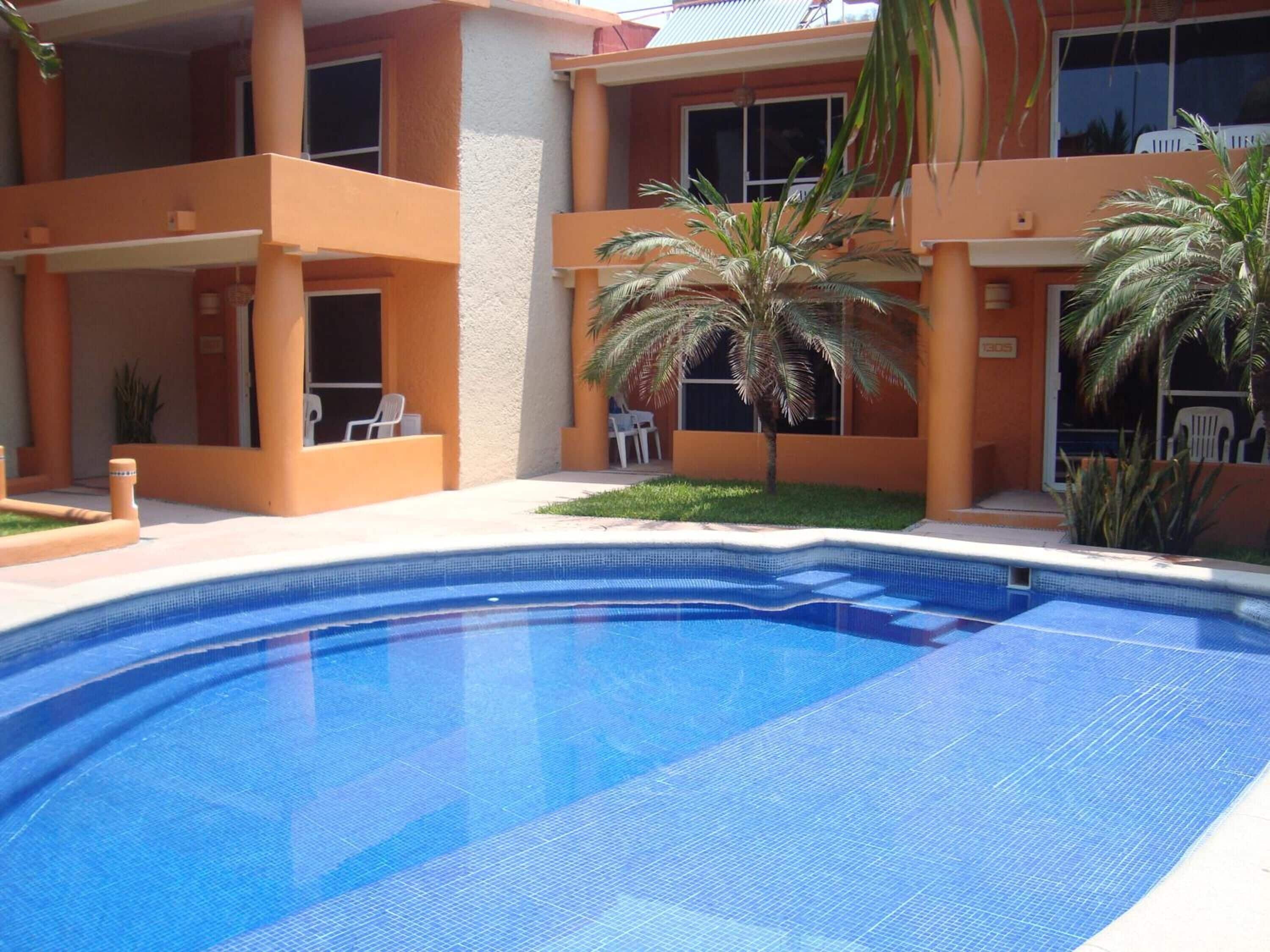 A swimming pool with a clear blue water surface, surrounded by a building with orange walls and multiple balconies.