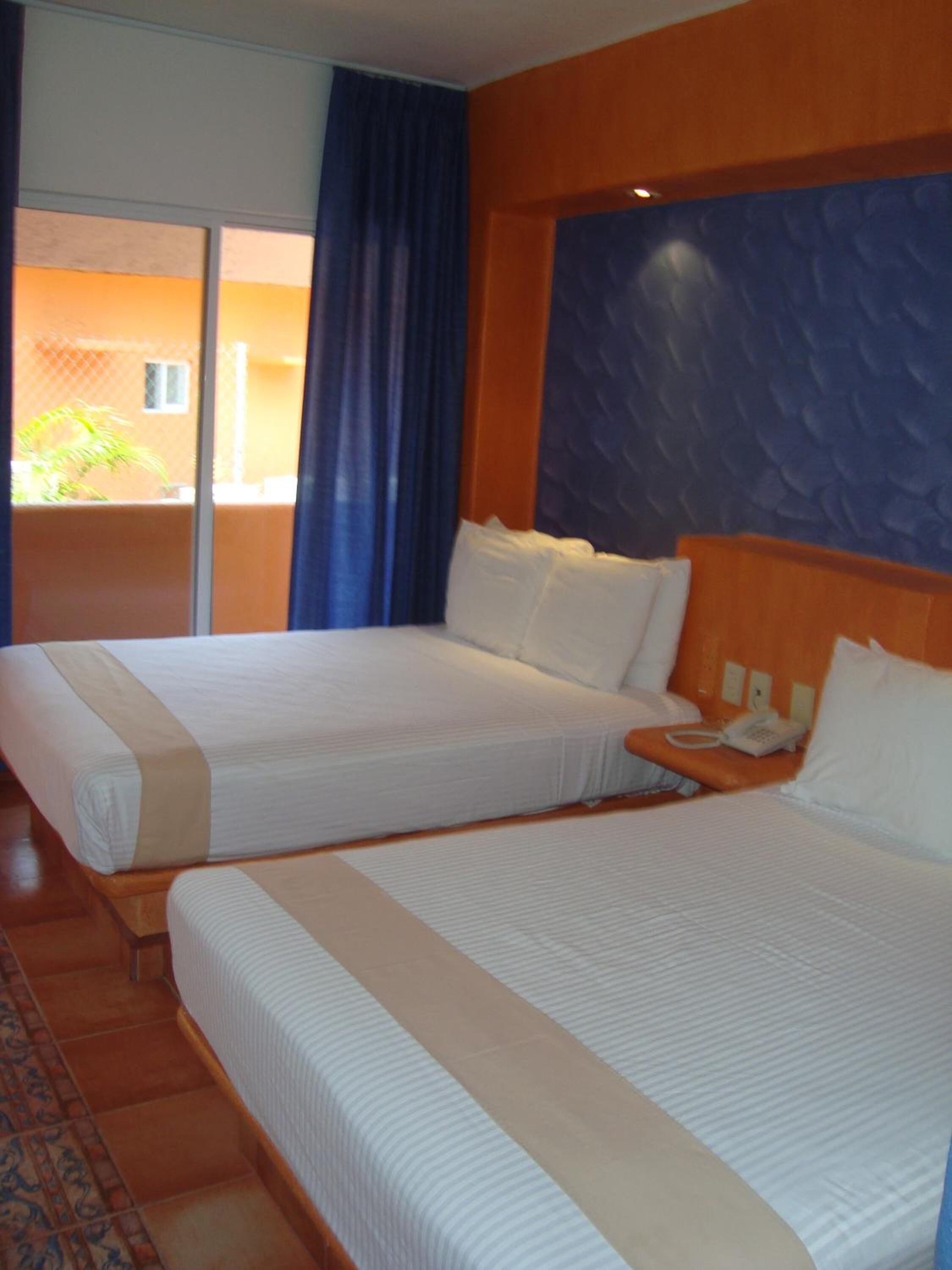 Habitación de hotel con dos camas, teléfono y vistas al exterior.