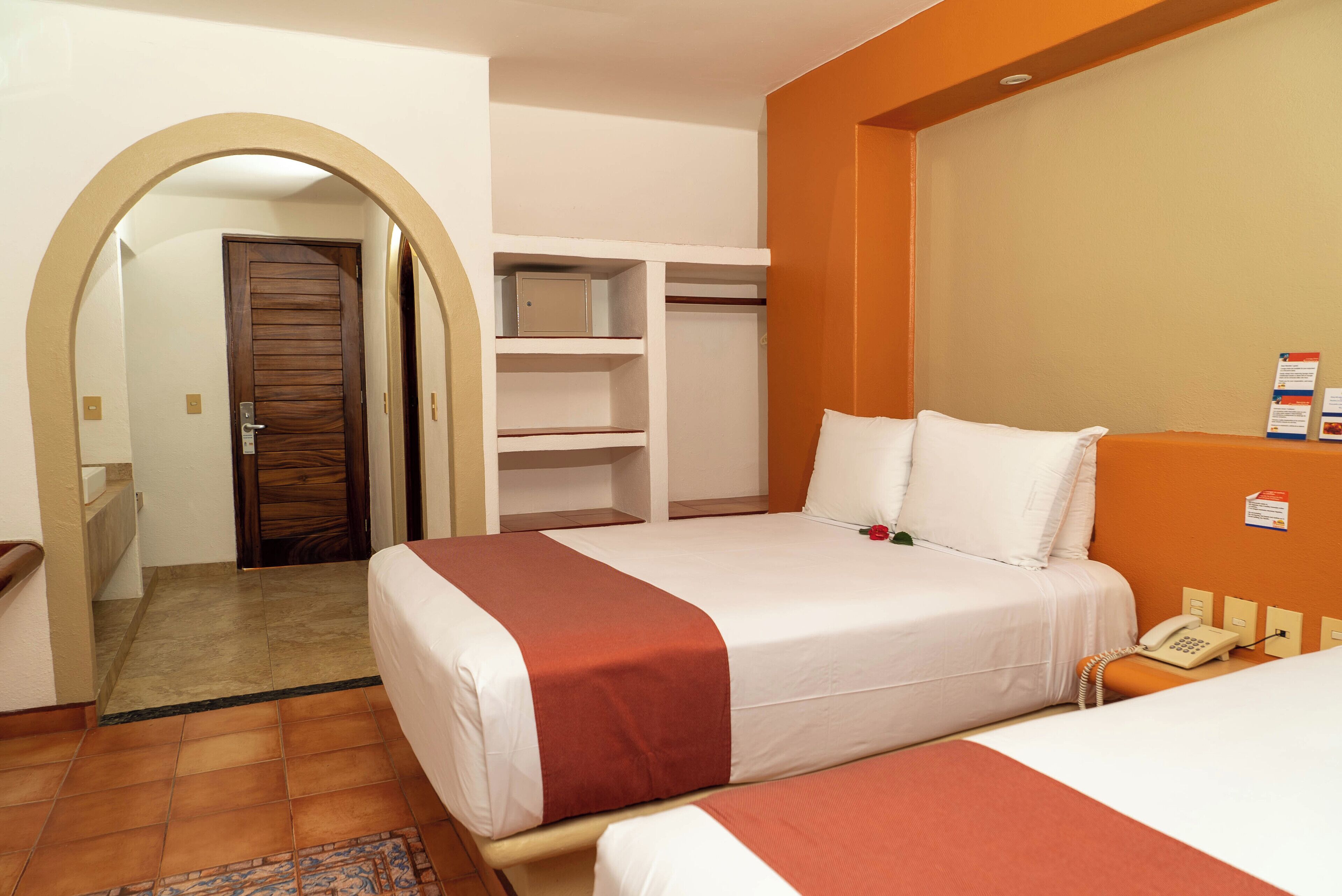 A hotel room with a bed, a telephone, a wardrobe, and a bathroom visible through an archway.