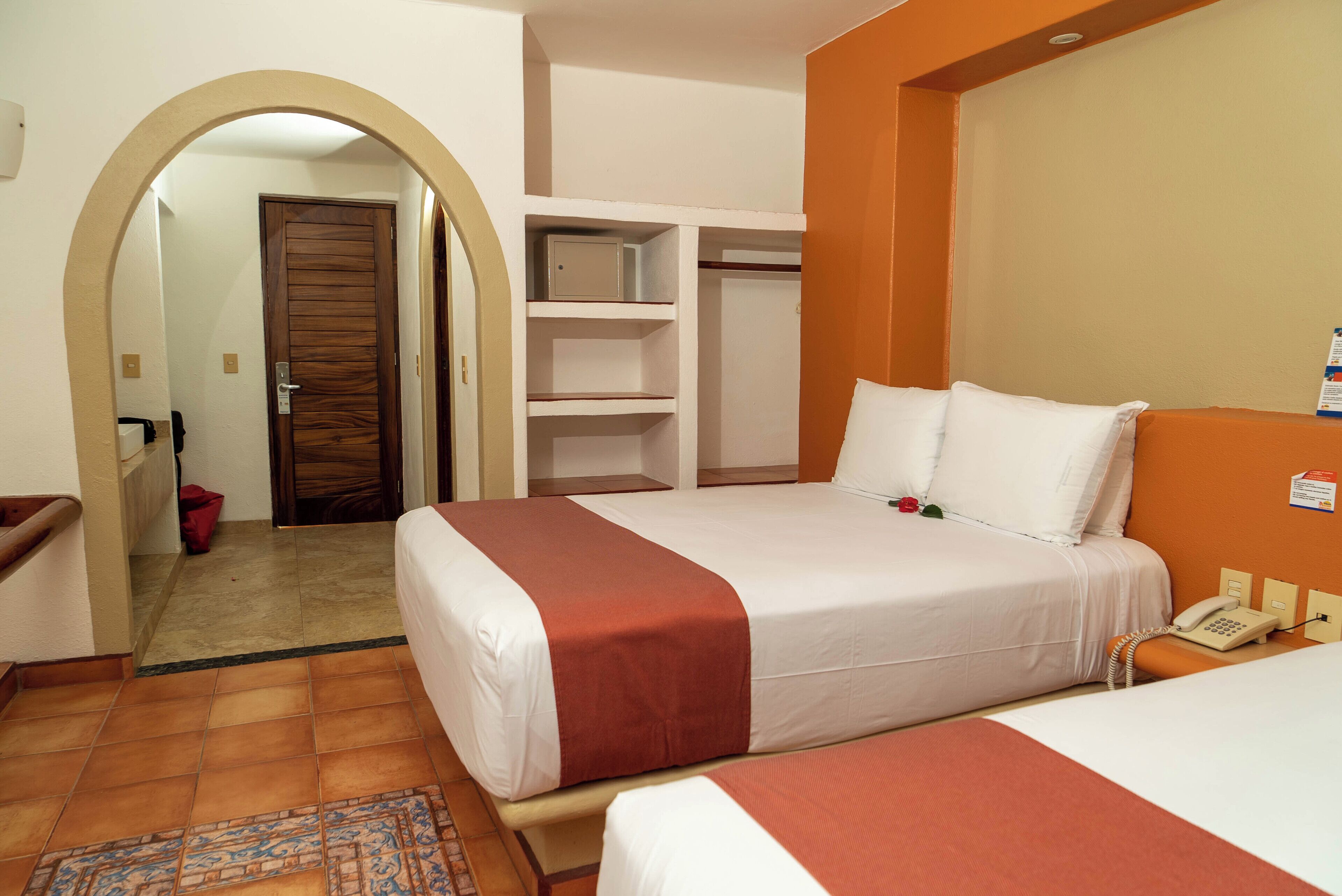 A hotel room with two beds, a wardrobe, a telephone, and a bathroom visible through an archway.