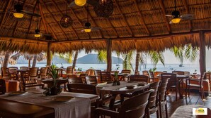 Un restaurante al aire libre con techos de paja, muebles de madera y vista al mar.