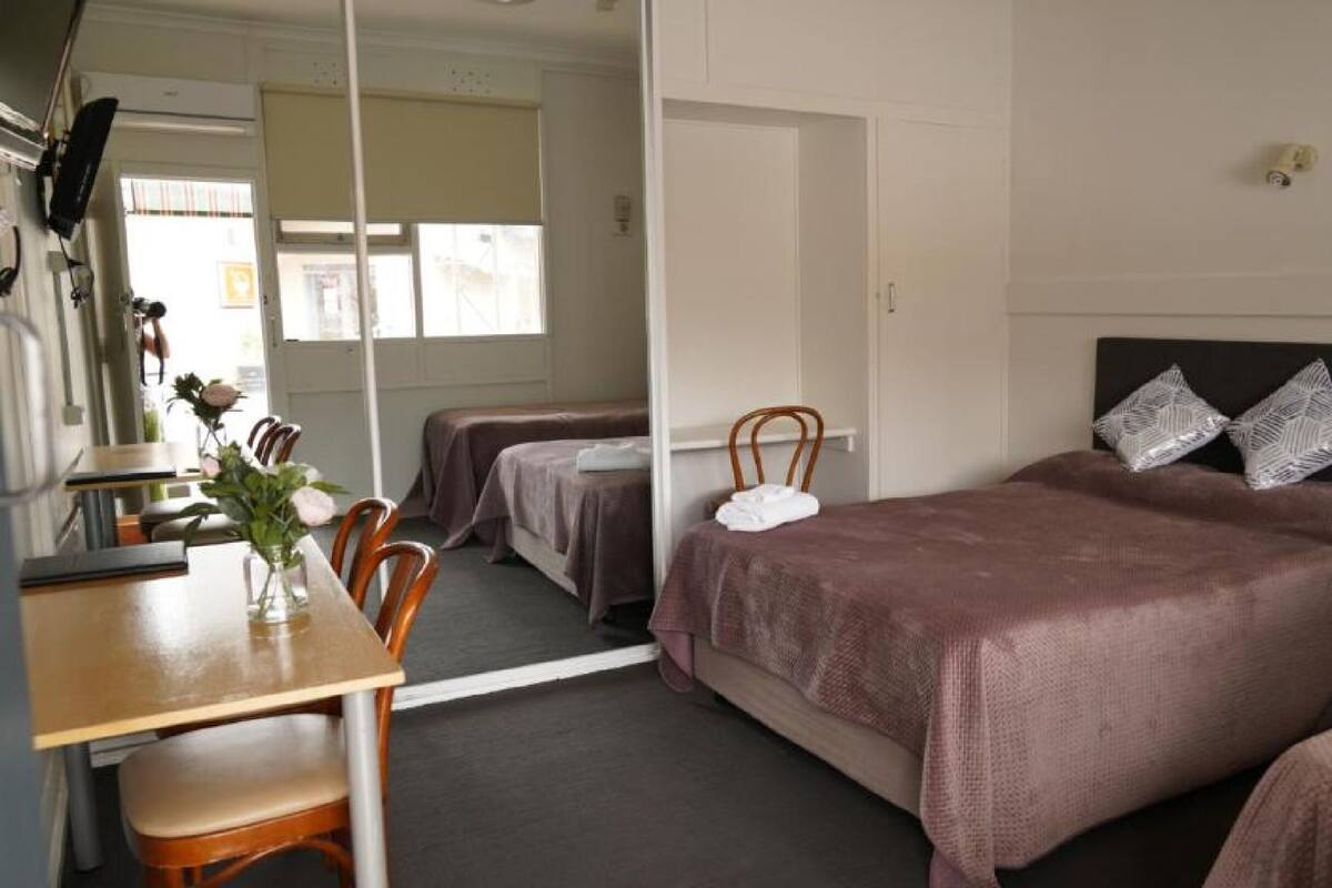 A hotel room with a bed, a desk, and a chair. There is a mirror on the wall, and a window with curtains.
