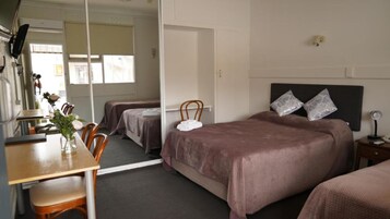Habitación de hotel con cama, escritorio y silla. Hay un espejo en la pared y una ventana con cortinas.