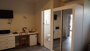 A compact hotel room with a kitchenette, a small refrigerator, a microwave, a wooden chair, a desk with a computer, and a sliding door leading to a bathroom. - Country Motor Inn Singleton (Singleton)