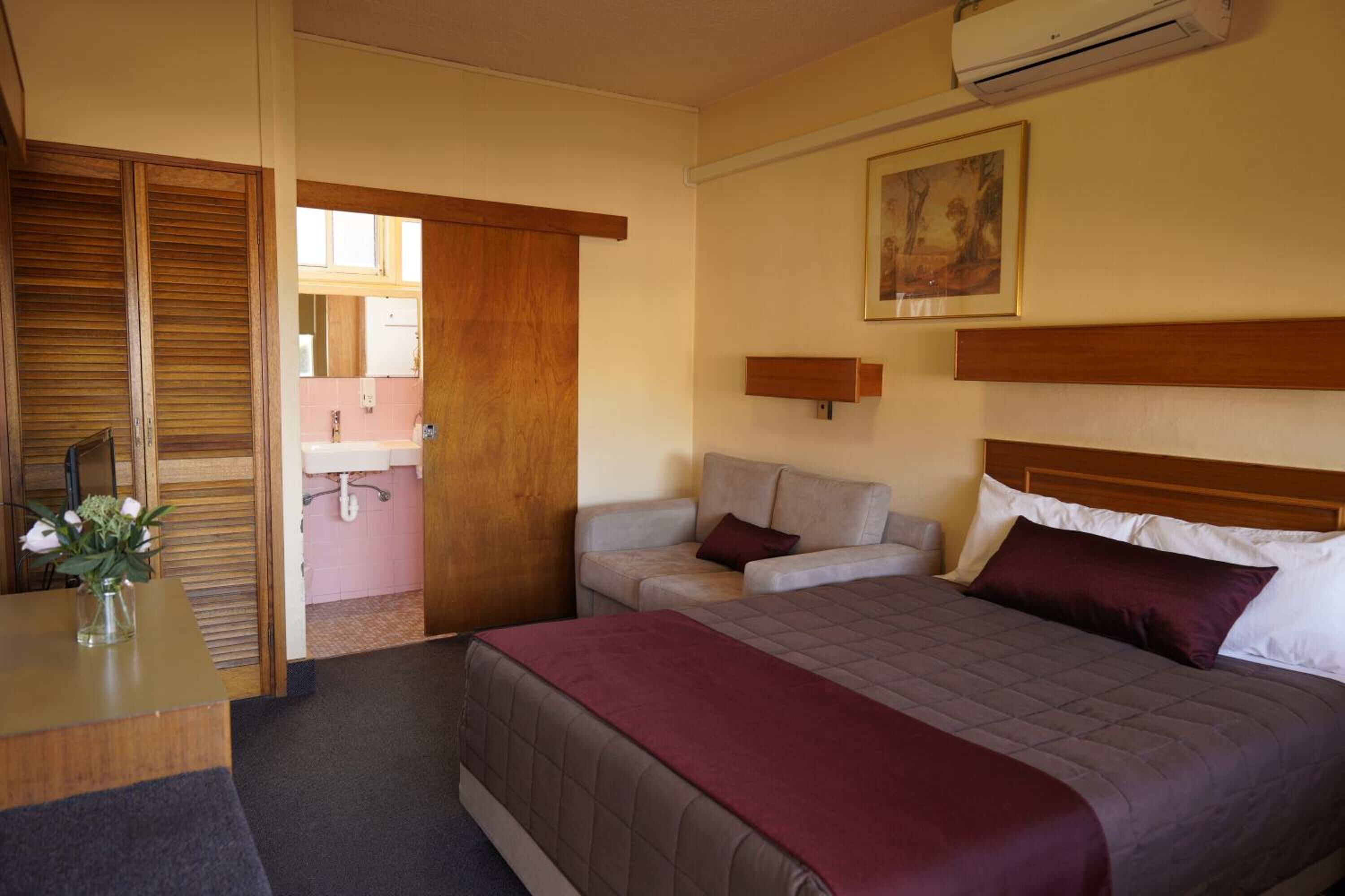 A hotel room with a bed, a desk, a chair, a sofa, and a bathroom visible through an open door.