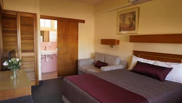 A hotel room with a bed, a desk, a chair, a sofa, and a bathroom visible through an open door.