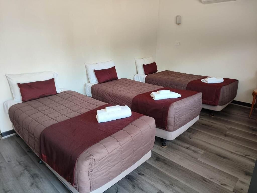 Habitación de hotel con tres camas individuales, cada una con colcha roja y almohadas blancas.