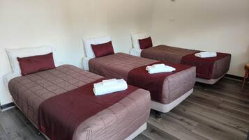 A hotel room with three single beds, each with a red bedspread and white pillows.