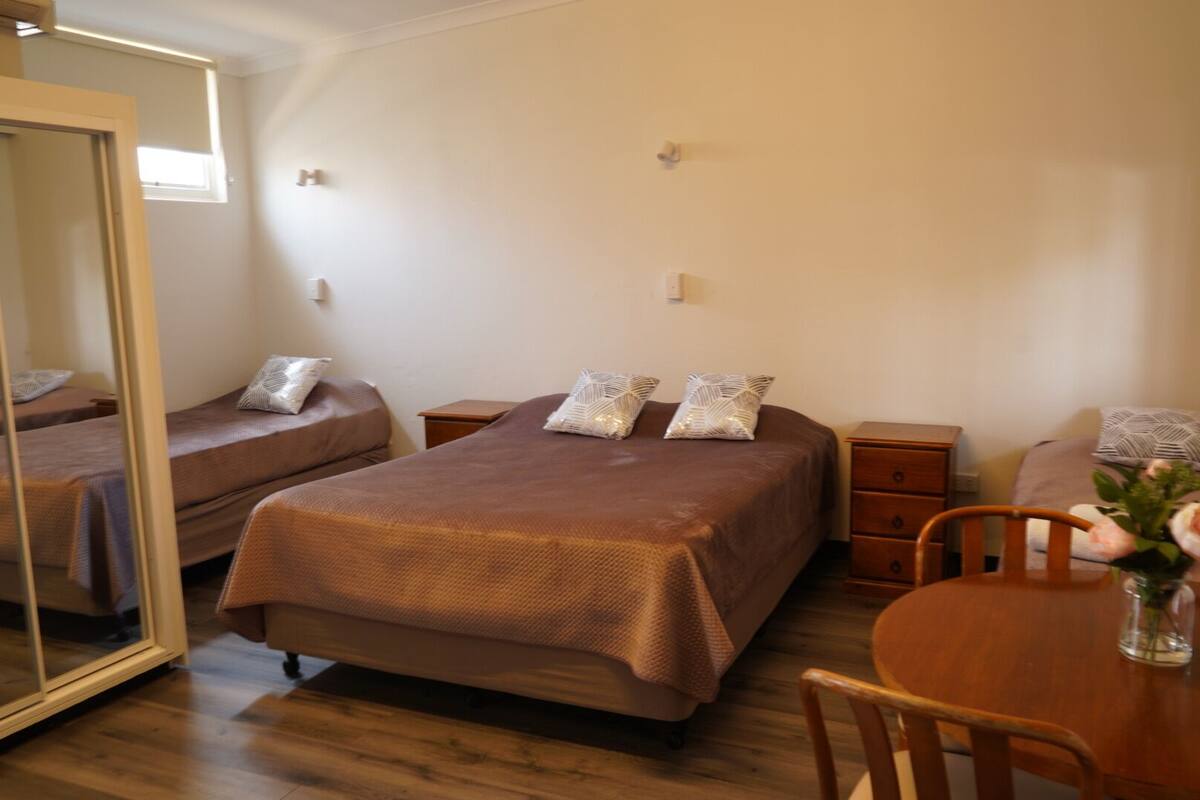 A hotel room with two single beds, a wooden dining table, and a mirror.