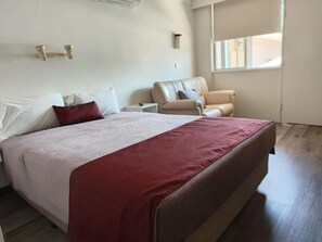 A bedroom with a bed, a nightstand, a chair, and a window.