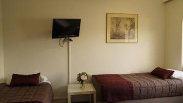 A hotel room with two beds, a TV mounted on the wall, a small table with a vase of flowers, and a framed picture on the wall.