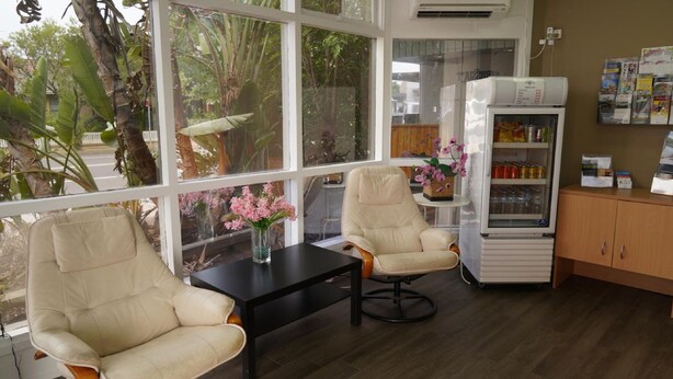 A room with two beige armchairs, a small table with a vase of pink flowers, and a refrigerator stocked with beverages. - Country Motor Inn Singleton (Singleton)