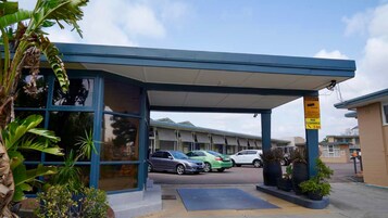 Un edificio con vestíbulo cubierto, un letrero de seguridad y automóviles estacionados.