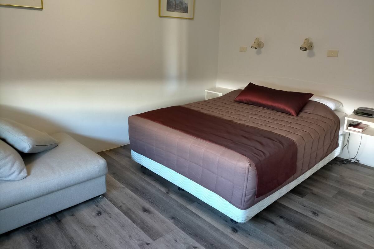 A bedroom with a bed, a bedside table, a nightstand, a lamp, and a chair.