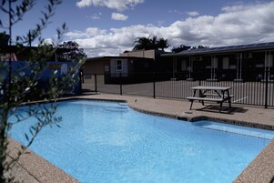 Una piscina con una mesa de picnic y un área cercada, rodeada de edificios.