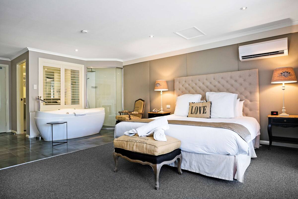 A modern hotel room with a large bed, a bathtub, a vanity, and a walk-in closet.