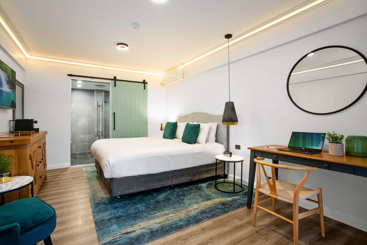 A modern bedroom with a bed, desk, chair, and a shower area.