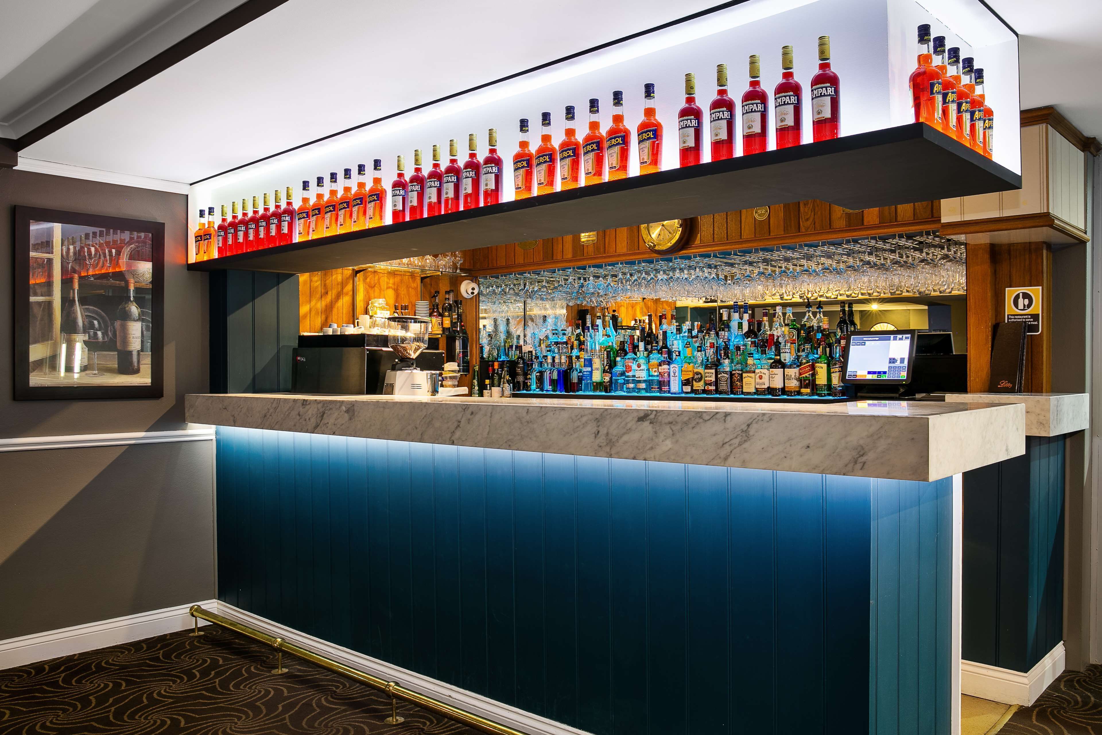 A bar area with a marble countertop, a variety of liquor bottles, and a digital screen.