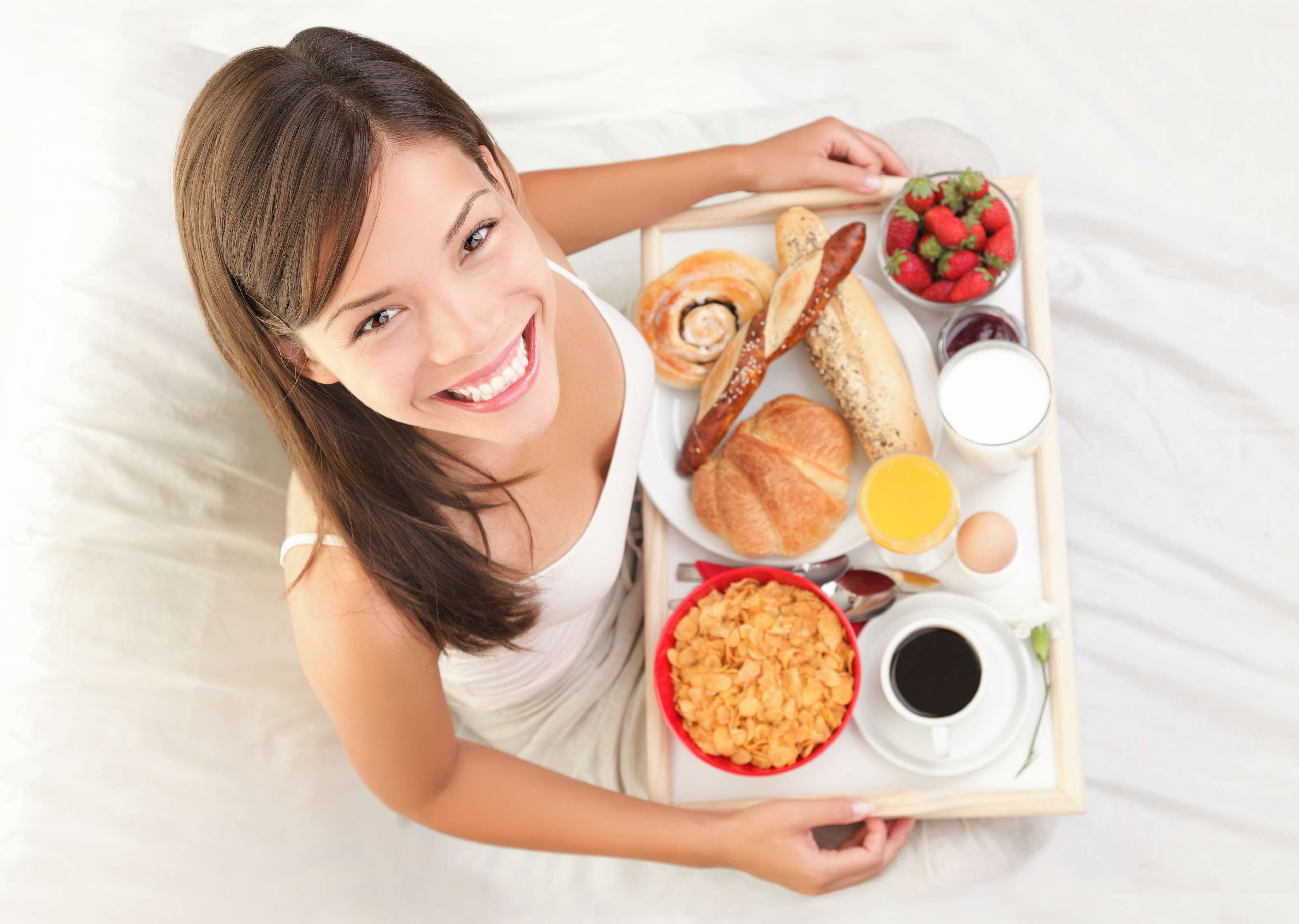 Een persoon houdt een dienblad vast met ontbijtproducten, waaronder croissants, aardbeien, ontbijtgranen en koffie.