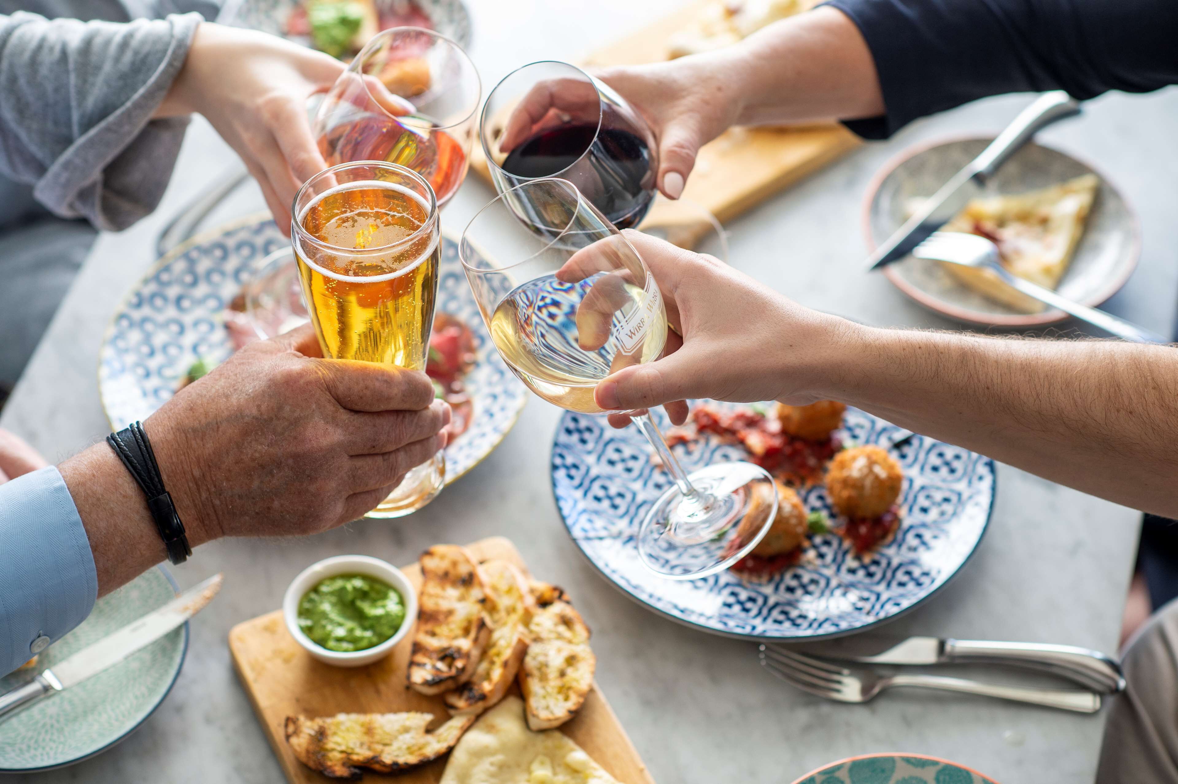 A group of people toasting with glasses of beer and wine at a table with food and drinks.