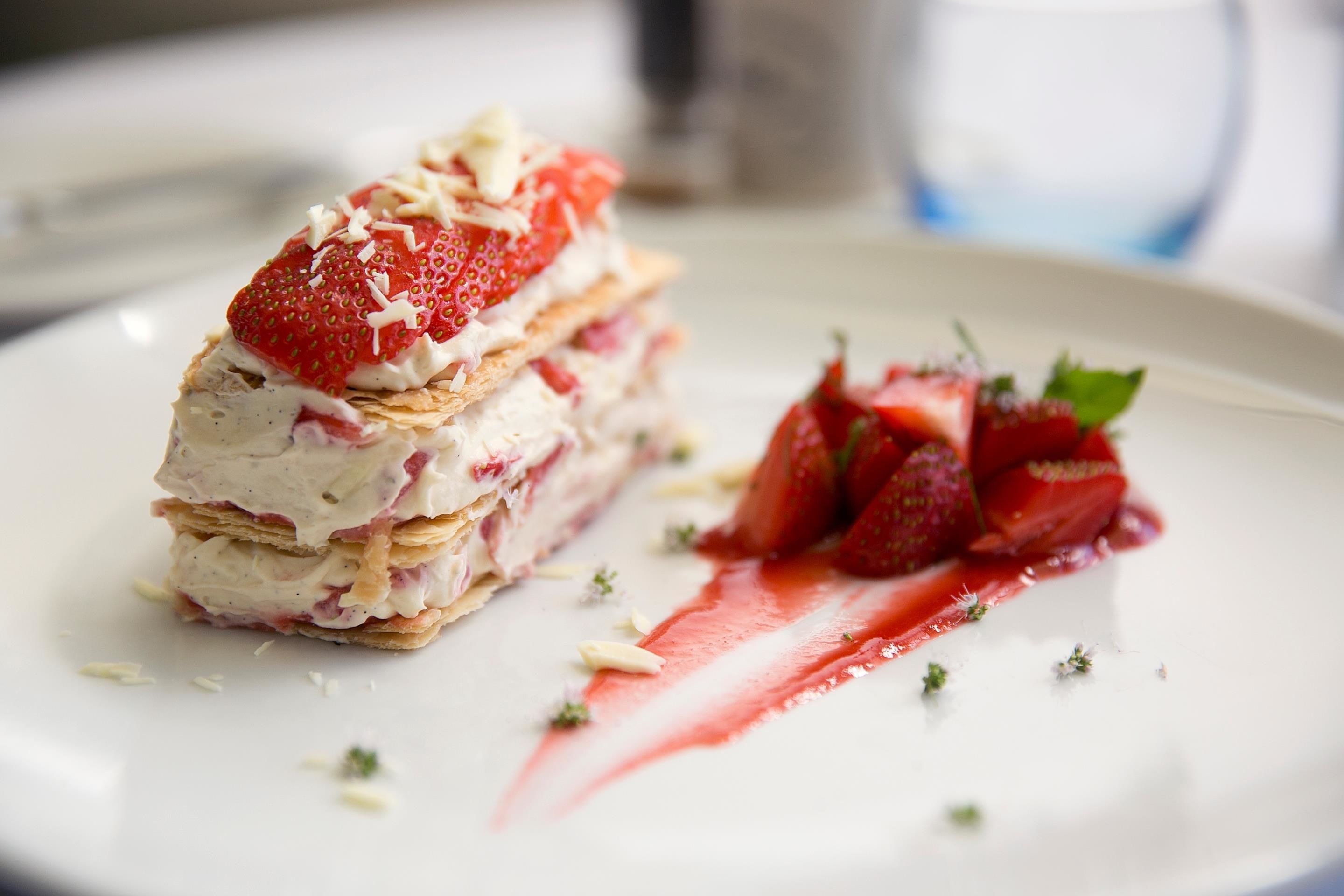 Een dessert met lagen room en aardbeien op een bord.
