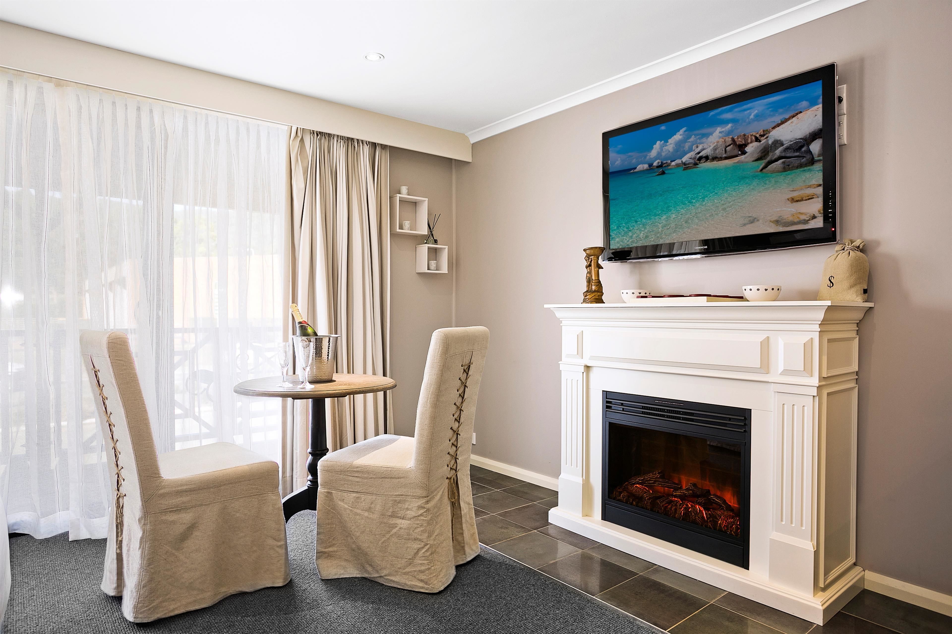 A living room with a fireplace, a television mounted on the wall, and two chairs.