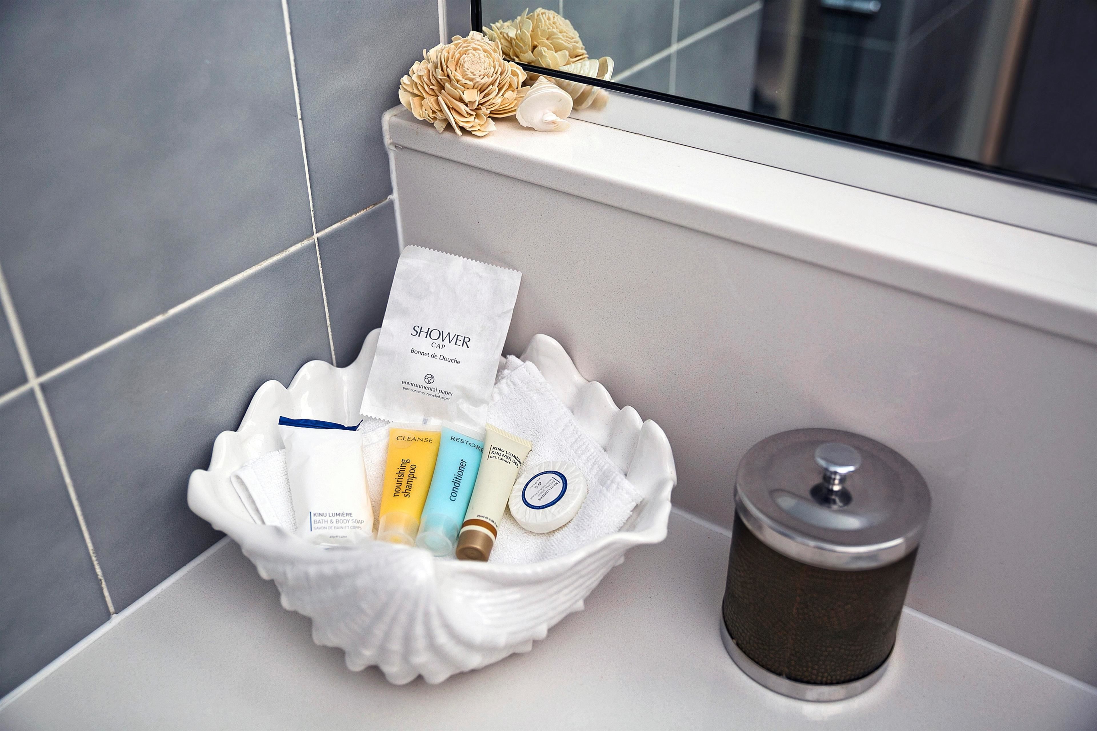 A bathroom with a white sink, a white bath mat, and toiletries in a white shell-shaped container.