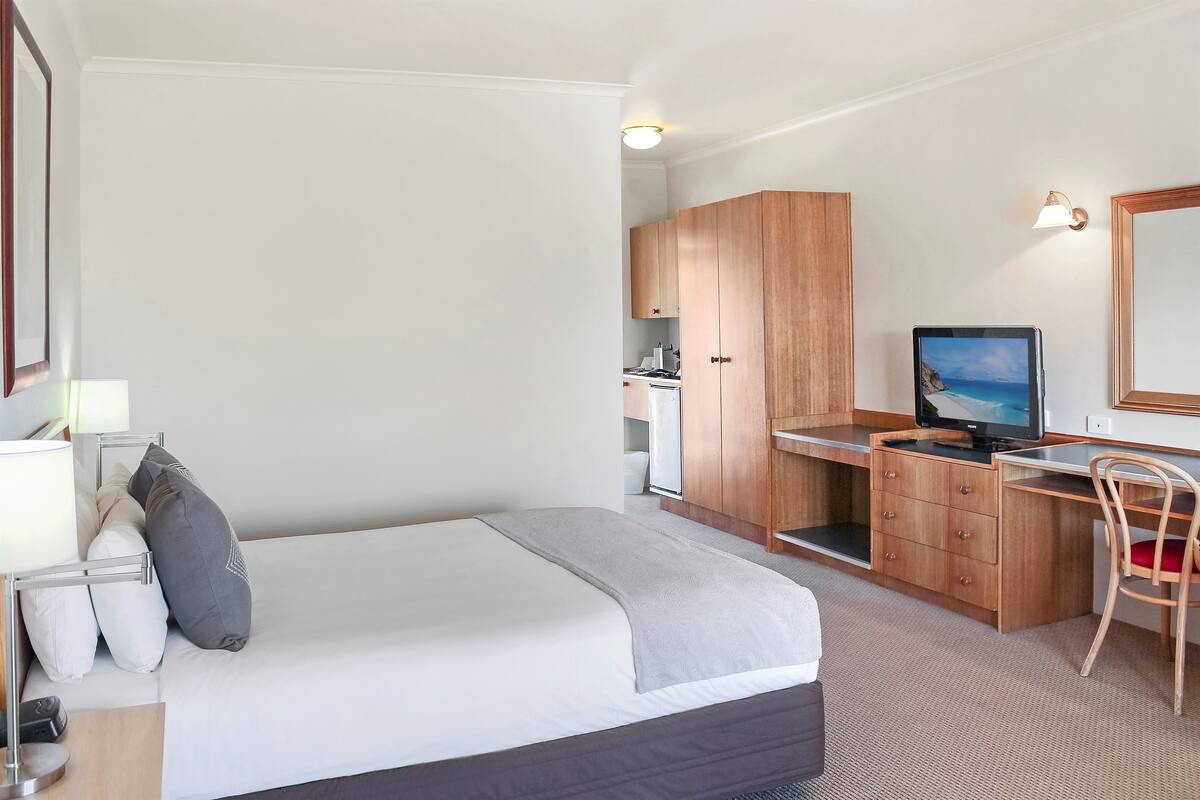 A hotel room with a bed, a desk with a computer, a chair, and a television.