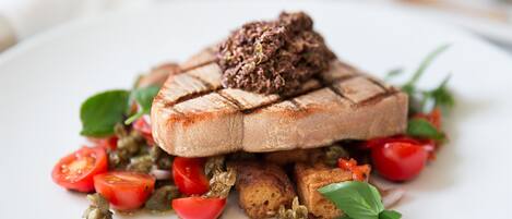 A plate with grilled meat, tomatoes, and a green sauce.