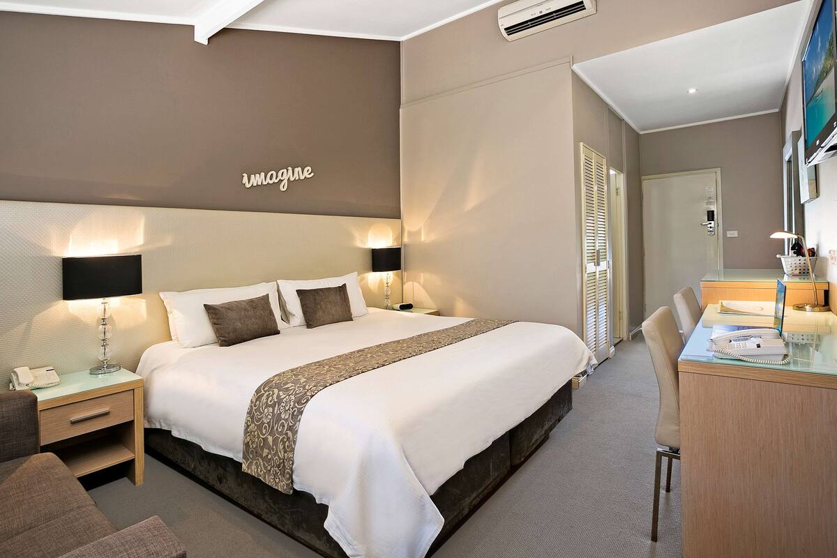 A hotel room with a large bed, bedside tables, a desk, and a mirror.