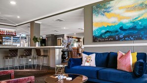 A modern hotel lobby with a blue sofa, a coffee table, and a bar area with stools. - Best Western Sanctuary Inn (Tamworth)