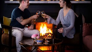 A couple toasting with wine glasses in a cozy room with a fireplace, a small table with a vase of flowers, and a shelf with candles and a rabbit figurine. - Best Western Sanctuary Inn (Tamworth)