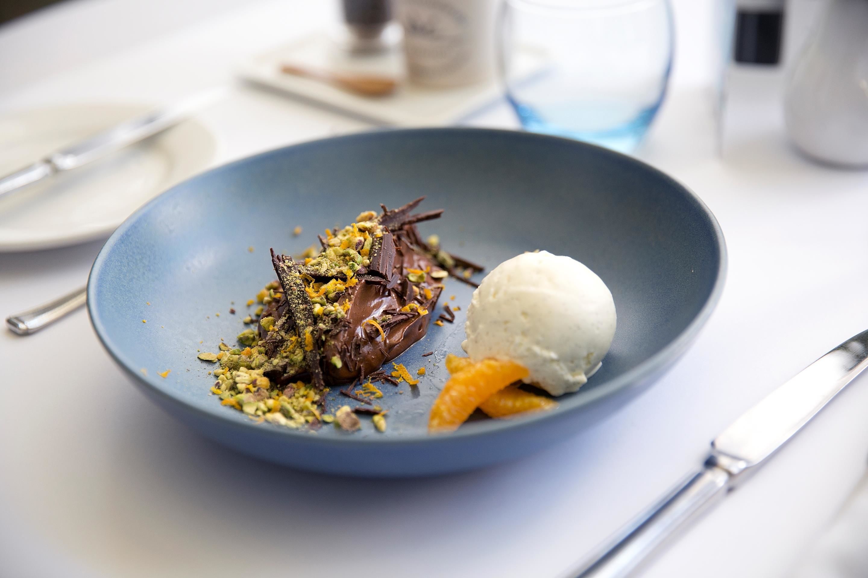 Un dessert servi dans une assiette bleue, composé d’une boule de glace et de quartiers d’orange.