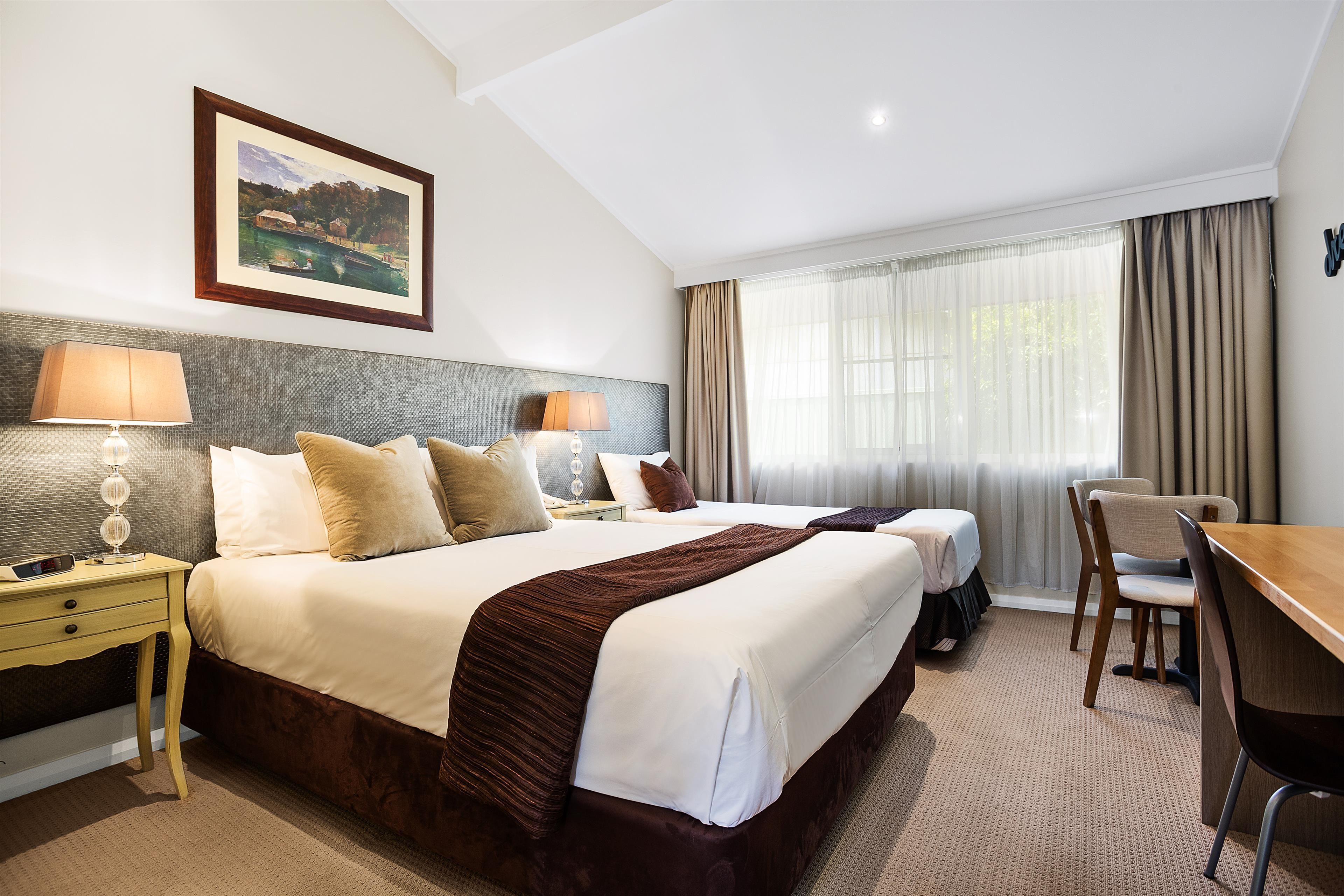 Una habitación de hotel con una cama grande, dos mesitas de noche con lámparas, un escritorio y una silla.