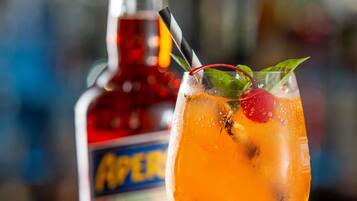 A cocktail in a stemmed glass with a cherry and mint garnish, and a bottle of Aperol in the background.